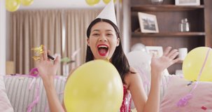 Video of smiling biracial woman in party hat and dressed in pink dress. Party, leisure time, domestic life and lifestyle concept.