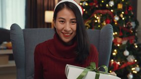 Attractive Asian female blogger smile looking at camera shopping online christmas show gift unbox review celebrated holiday video conference call surprise follower in social media platform at house.