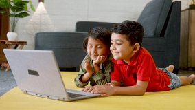 young kids watching videos on laptop by clapping while sitting on floor at home - concept of leisure activity, technology addictions and relationship.