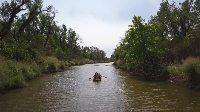Slow tracking shot of people kayaking down a brown river after rainfall