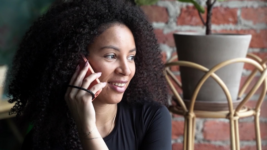 Happy woman with African curls speaking on cellphone at home or cafe indoors. Communication with friends of relatives. Comfort relationships.  | Shutterstock HD Video #1096877165