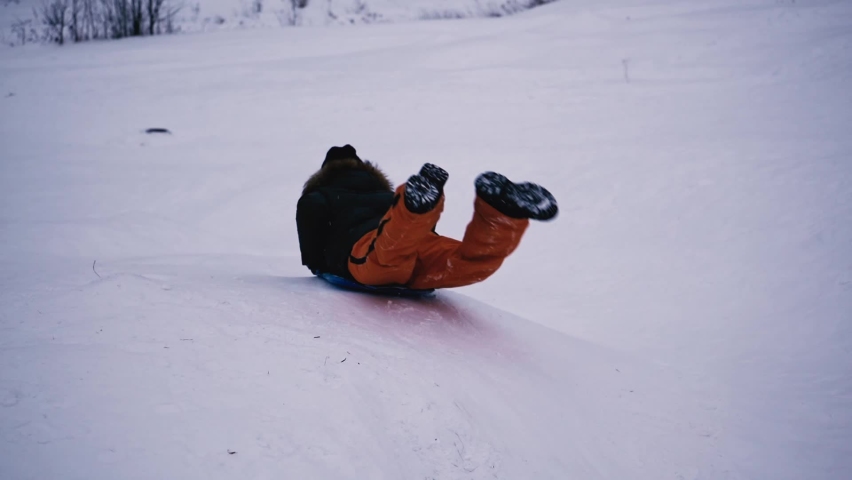 The boy rolls down the snowy slope on an ice rink, a sled. Winter fun Royalty-Free Stock Footage #1096877663