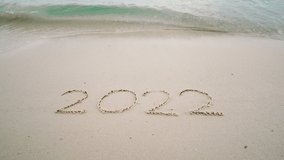 4K happy new year 2023. number 2022 write on sandy beach, ocean wave splash change to 2023. countdown for happy new year turning from year 2022 to 2023 video footage background
