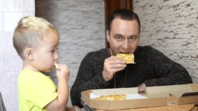 Caucasian kid boy and his father eating pizza. Father feeds his son with fast food, unhealthy food concept. Horizontal 4k footage, family breakfast morning