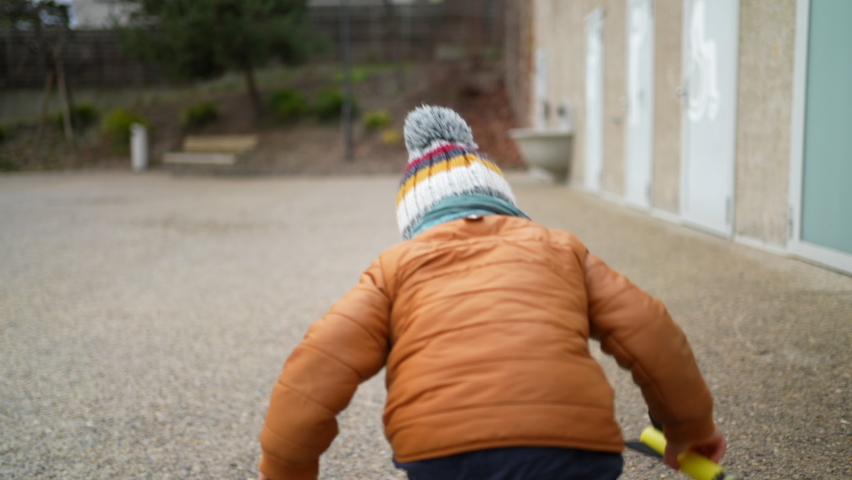 One small child running outside at city park during winter season. Little boy wearing beanie hat and jacket