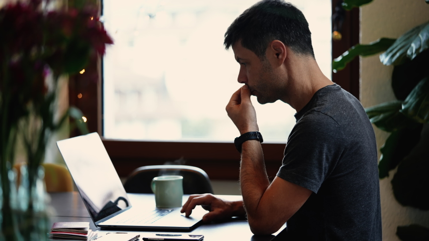 Candid thoughtful man working from home in front of computer. Concentrated person using modern technology works remotely