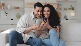 Happy cheerful woman and man Hispanic Latino married couple looking at smartphone smiling talking watching funny video photo sitting on couch at home online fun mobile app using cellphone laughing - Powered by Shutterstock - Get 15% off with code: PIKWIZARD15