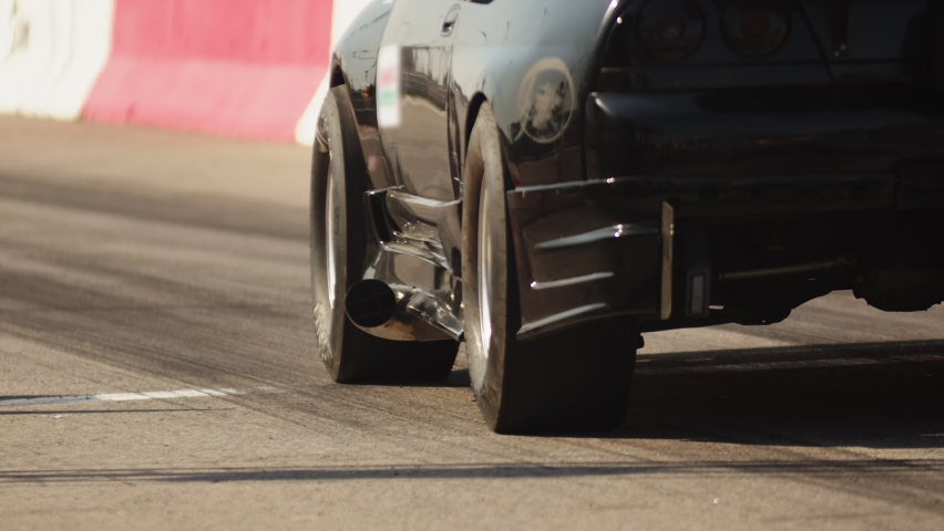 Sports black car is accelerating. Back view. A racing car with a powerful engine starts on the track. Tire friction on asphalt