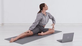 A strong beautiful fitness girl in training clothes does yoga stretching exercises in the gym, uses a digital tablet for online exercises, workouts, streaming fitness.