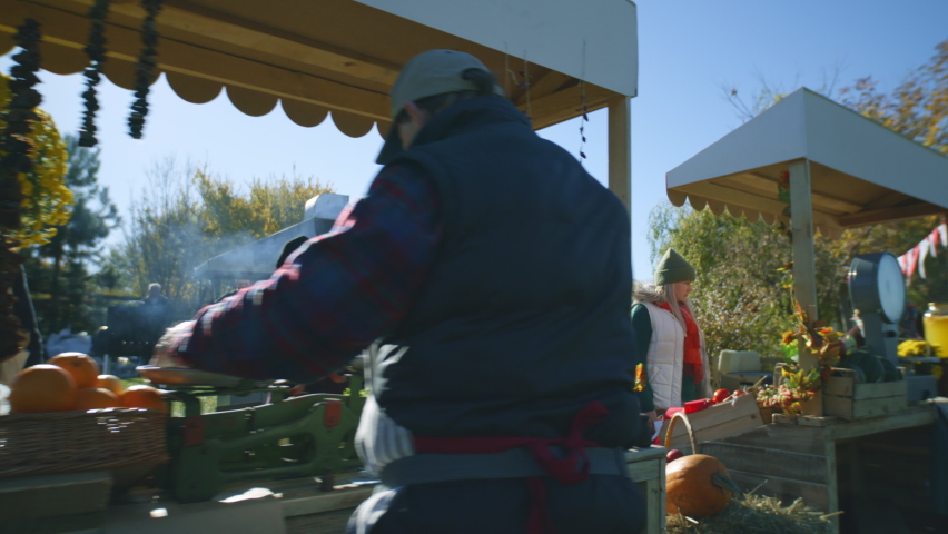 People walking, shopping, choosing fruits and vegetables at local farmers market. Autumn fair, weekend activity. Vegetarian and organic food. Agriculture. Points of sale system. Woman with kids.