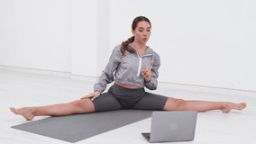 A young beautiful female trainer, stretches and practices stretching and yoga with a student through a video call in a bright sunny gym. The concept of a healthy lifestyle, fitness, well-being