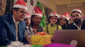 Happy smiling modern Asian Indian family members wearing Santa caps interacting or talking online with distant relatives on a laptop during Christmas eve holidays. celebration, connectivity concept.