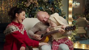 Happy family celebrate christmas eve together at home at decorated background. Mother and father spend time with a cute son teaching to play guitar, listen music. Christmas new year, loving parents - Powered by Shutterstock - Get 15% off with code: PIKWIZARD15