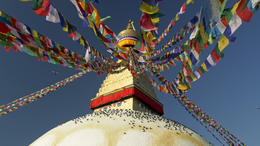 Boudhanath stupa in Kathmandu, Nepal. Camera moves between Buddhist flags swaying in the wind, pigeons sit on the dome of Boudhanath Pagoda. UHD, 4K gimbal shot, slow motion