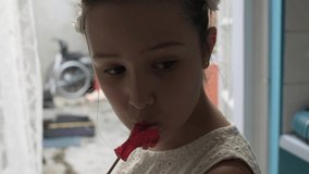 Happy schoolgirl in white wreath of flowers. Beautiful Girl emotional face indoors close-up. Dream young girl at home. Funny kid licks candy on stick. Child smiles at camera. teenager eats lollipop