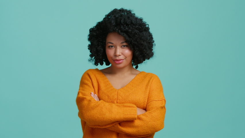 Playful African American model looking straight to camera with flirting eyes and mysterious smile on beautiful face. Multi ethical curly woman pretending to be serious with crossed hands on chest