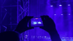 Tourist visits concert recording video of good memories on smartphone. Person holds phone and enjoys concert. Visitor admires show view in dark premise