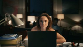 Focused girl speaking computer at cozy home. Serious woman solving tasks at laptop. Busy lady talking with client closeup. Skilled freelancer working overtime. Man silhouette sitting at background