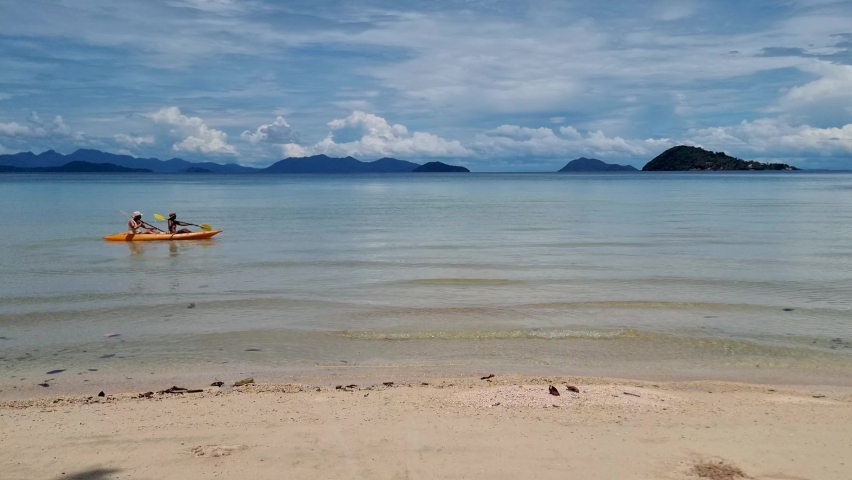 Couple mid age men and women paddling in Kayak in the ocean of the tropical Island of Koh Mak Thailand. men and women in kayaks at a blue ocean and white beach with palm trees