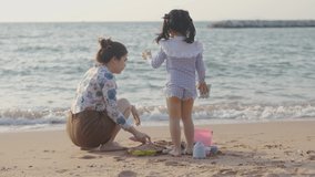 Video footage 4k of Asian cute little girl and her mother playing or making sand castle with sand on tropical beach. Children with beautiful sea, sand blue sky.