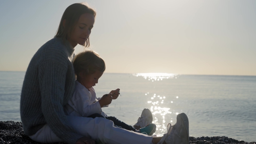Mother playing with baby at the seahorse, beautiful sunrise, , woman embracing little child, parent love, sun shining over sea. High quality 4k footage