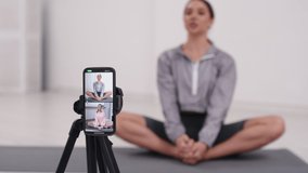 Cinematic shot of young athletic european woman with athletic body doing leg and butt exercises on fitness mat with online student in stretching and yoga room
