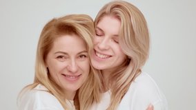 Tender young and beautiful european women embracing and smiling. Portraits of blondes mother and daughter, studio shot, white background. Happy two generations, women family. High quality 4k footage