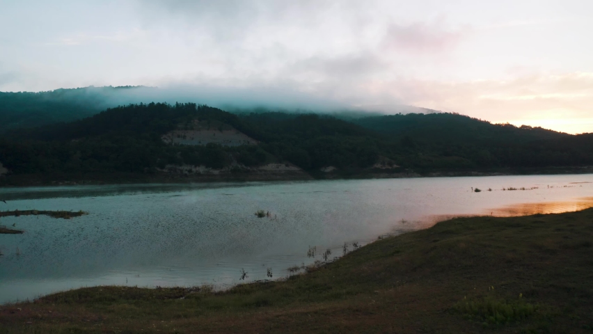 Fog on the lake. Golden sunlight rising, moving orange mist on water surface in summer. Forest background and beautiful calm reflections