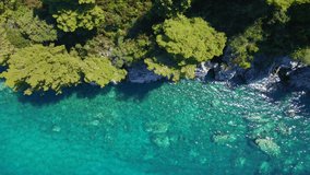 Aerial slowmotion video. Top down view on a rocky shore with beautyful clear sea and rocks covered with pine trees