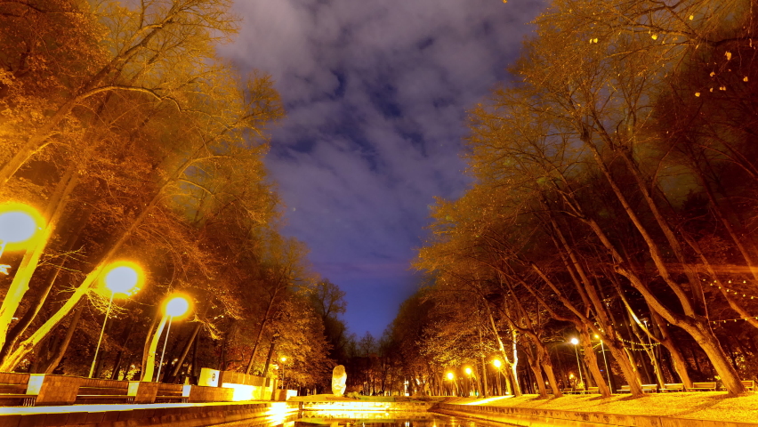 4K timelapse of northern Europe city park in autumn. Yellow light anterns around mountain. Dynamic movement of clouds in the sky. Monument and fountain in the centre.