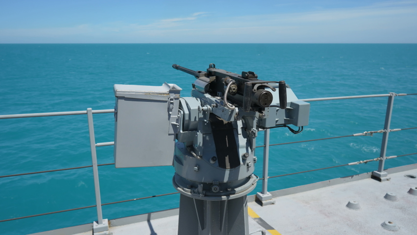 Color footage of an automated machine gun on the deck of a military ship, at sea.
