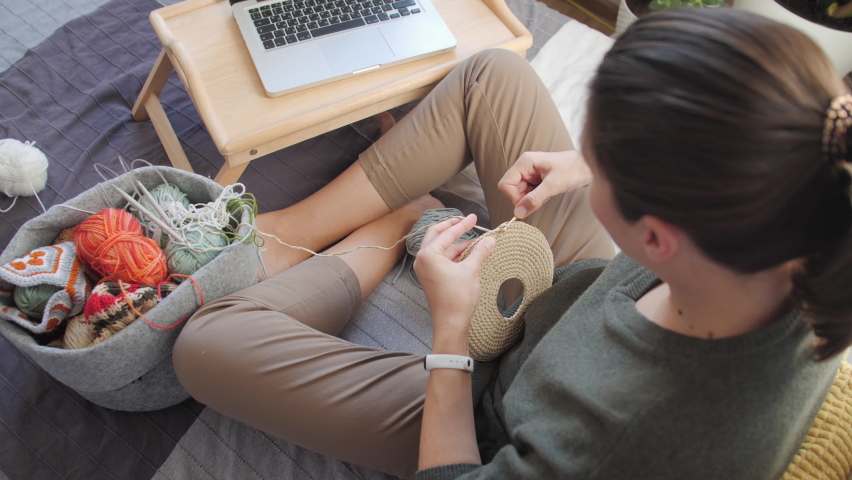 Close-up video of woman learning to crochet. Felt basket with balls of yarn. Anti-stress hobby. Online lessons for amateurs on laptop.