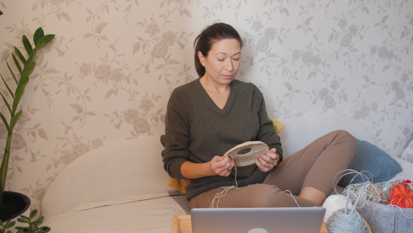 Close-up video of woman learning to crochet. Felt basket with balls of yarn. Anti-stress hobby. Online lessons for amateurs on laptop.