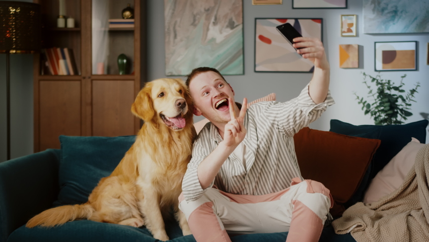 British redhead man together with dog retriever making selfie photo or video call on front camera smartphone. Positive young student man conference call with pet for blog.