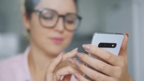 Woman in eyeglasses smiling, searching and watching funny videos on smartphone