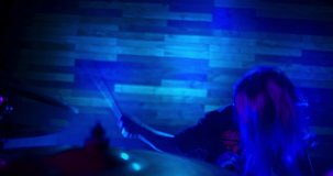 Professional drummer energetically playing drums in twinkling strobe lights. Makes beats on a metal Crash cymbal. Girl drummer concert concept. Waves hair in slow motion.