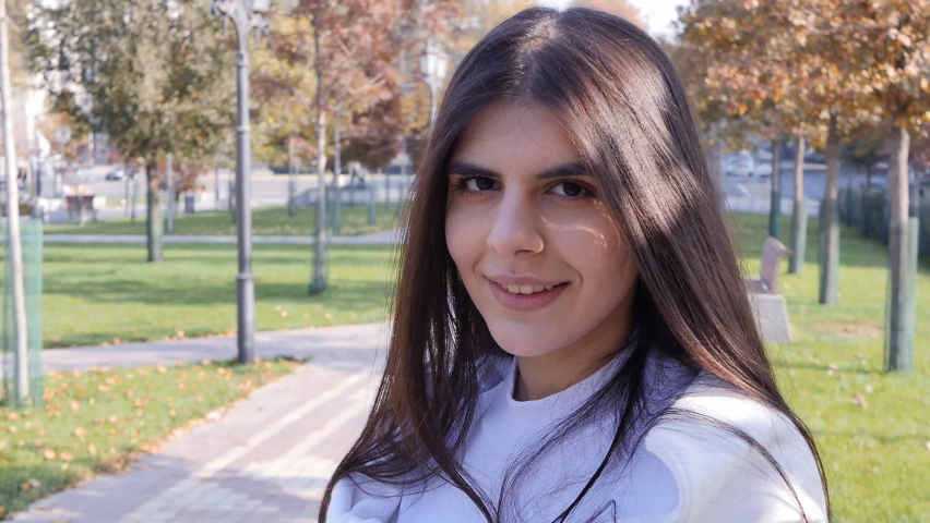 Portrait of a beautiful young girl with black hair and black eyes of the Middle Eastern ethnic group. Pretty brunette smiles sweetly and looks into the frame while standing in the park on a sunny day