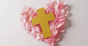 Video of yellow christian cross on heart shape of pink rose petals on white background. Love, faith and religion concept.