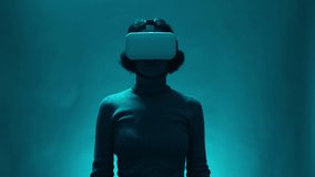 Female model with VR headset user in digital interactive performance, entertainment of future, technology. Mature woman uses virtual or augmented reality glasses in magic atmosphere of teal blue light
