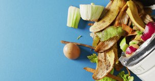 Video of organic, fruit and vegetable waste spilling from kitchen composting bin. On blue background with copy space. Ecology, recycling, care and nature concept.