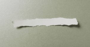 Video of close up of torn piece of white paper on green background. Paper, writing, texture and materials concept.