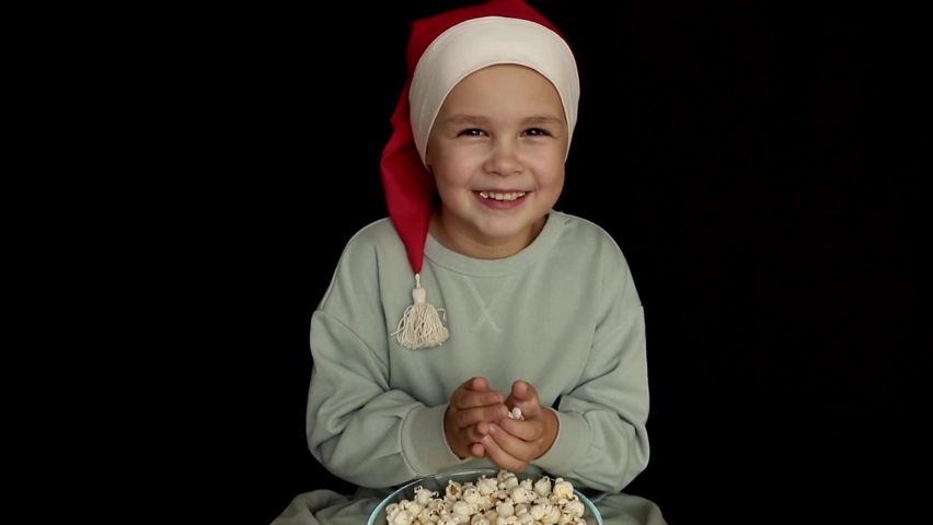 a little girl in Santa's hat. A child eats popcorn. It's Christmas time. The child laughs. Kids throw popcorn Royalty-Free Stock Footage #1096952261