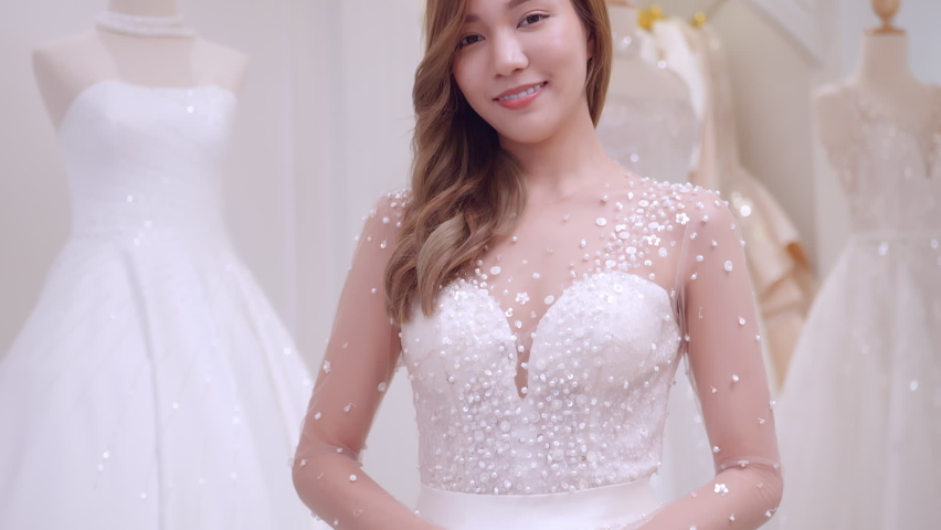 Young Asian bride trying on wedding dresses in wedding studio.	
