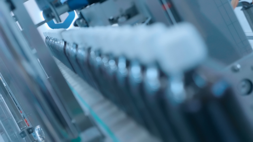Industrial line of food, medical or chemical industry for filling liquids into glass or plastic brown transparent bottles with white caps. Closeup