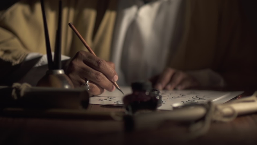 A medieval man uses an old pen with ink to write Arabic script on an a paper lit by a candle,slow motion