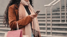 Unrecognizable woman shopper unknown girl in trendy coat stylish fashionable scarf walking in city holding shopping bags packages purchases chatting browsing smartphone mobile phone online discount - Powered by Shutterstock - Get 15% off with code: PIKWIZARD15