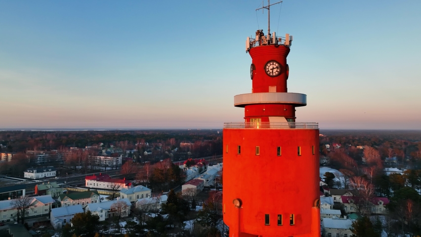 Aerial view in front of the sunlit water tower revealing the church, sunrise in Hanko city, Finland - reverse, pan, drone shot