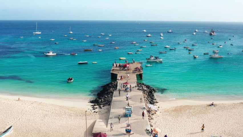 Flying over the pier in Santa Maria, Sal Island - Cape Verde.
Aerial 4K UHD drone view of fishermen boats at tropical island. Colorful turquoise ocean.