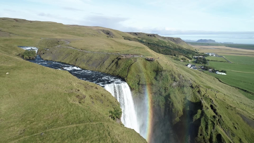 Iceland near Skogafoss waterfall. Powerful river water falls down the cliff and cloud of water drops is covering the waterfall. In the cloud you can see small rainbow.
