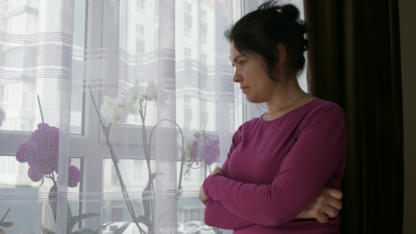 Concerned Distressed Woman Stands Thinking Looking out of Window. Sad Expression Upset Female Emotions. Housewife Wife Calms Down after Stress. War in Ukraine Crisis.  Royalty-Free Stock Footage #1096965435